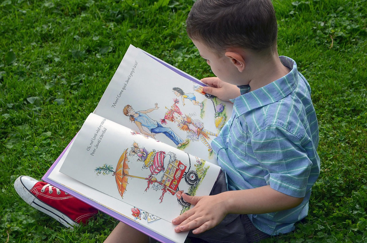 Young boy reading a colorful picture book outdoors, enjoying fun illustrations and storytelling.