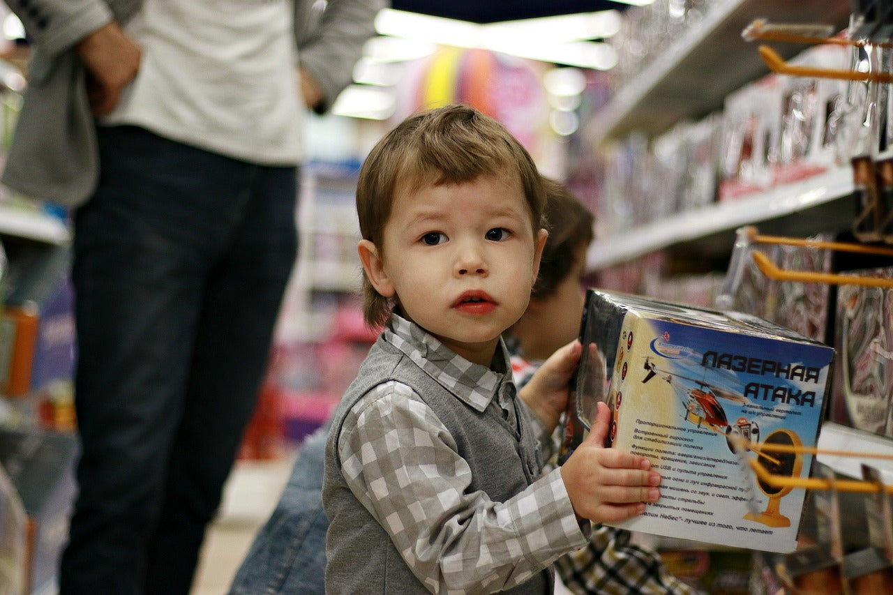 Young child shopping in a toy store holding a boxed toy helicopter, exploring fun gift options for kids.