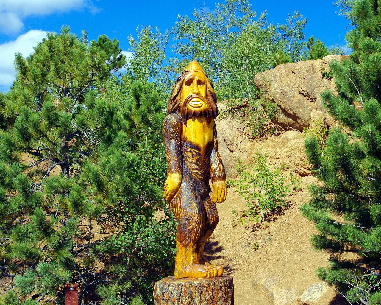 Wooden Bigfoot statue in a forest setting promoting Bigfoot Books collection with adventure and mystery themes.