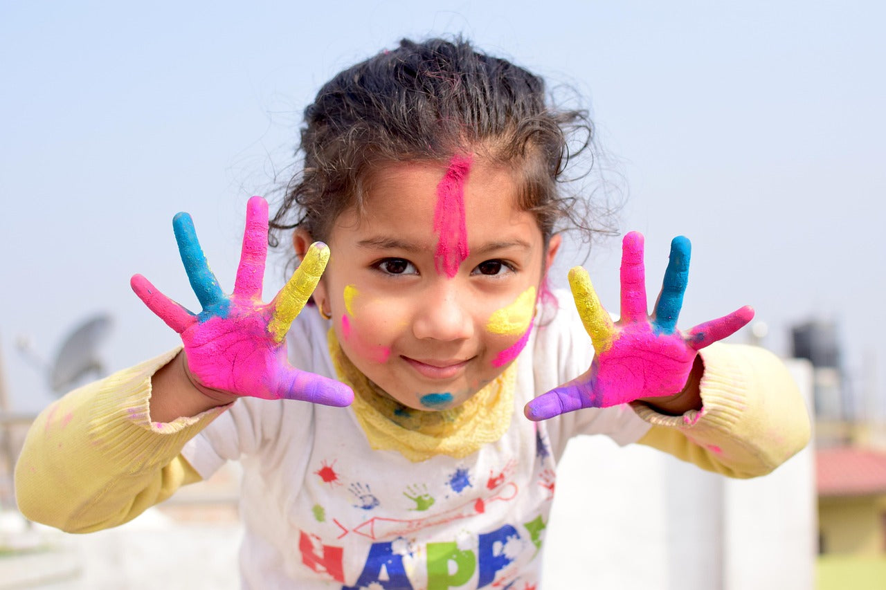 Smiling child with colorful paint on hands and face enjoying fun learning activities from Kid Scoop Books.