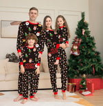 Family of four wearing matching Christmas pajamas in a living room with a decorated tree.